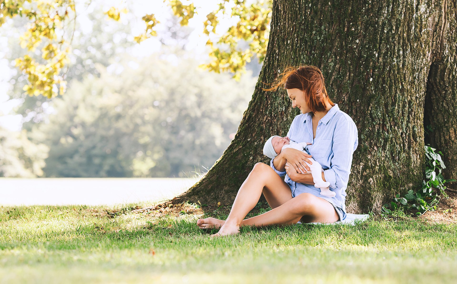 Mama siedzi z dzieckiem na trawie pod drzewem